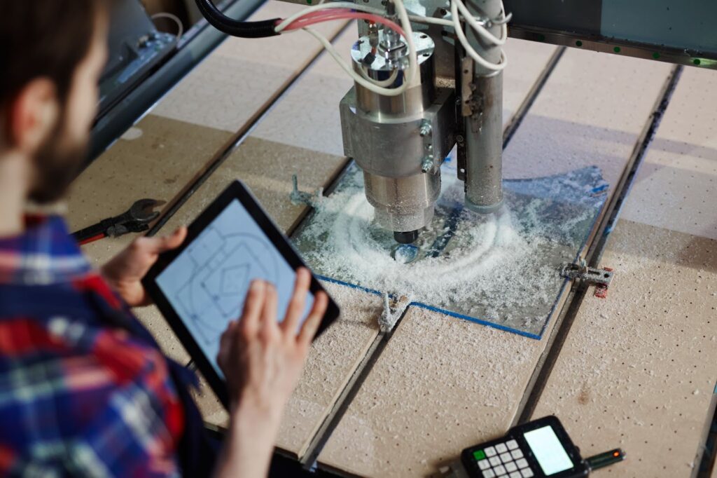 a man holding a tablet and watching a CNC machine in action